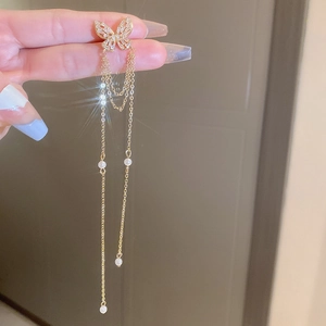 Macro shot of gold butterfly tassel earrings with sparkling zircon and pearl accents