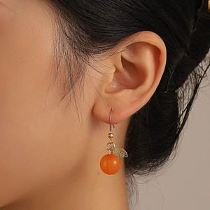 Close-up of realistic orange fruit earrings with green leaves on a gold metal hook