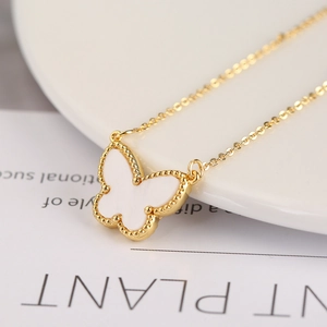 Macro shot of a golden butterfly pendant necklace with white inlay and beaded edges