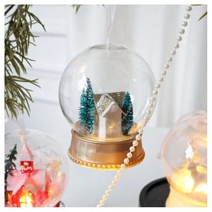 Macro detail of LED Christmas bauble with miniature snowy house and pine tree forest