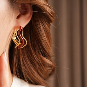 Close-up of red and gold wavy hoop earrings with enamel finish on a fashion model