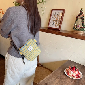 Close-up of yellow and blue striped plush crossbody bag worn by a model in a cafe