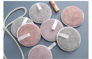 Three-layer charcoal fiber makeup remover puffs in pink and grey on a decorative background