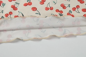 Detailed view of cherry print fabric with lettuce edge hem on a beige summer top
