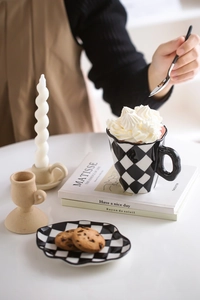 Macro shot of ceramic checkerboard cup and saucer with cream-topped coffee and cookies