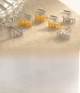 Detailed view of titanium steel nose studs with her, him, and them letter designs