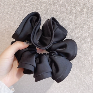 Detail view of a large black satin scrunchie showing glossy fabric texture and ruffles