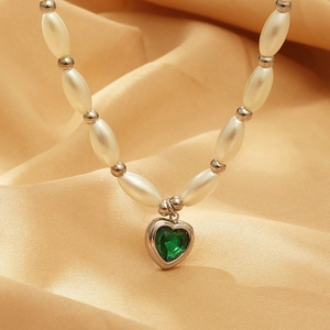 Detail of beaded necklace with faux pearls and a green heart-shaped crystal pendant