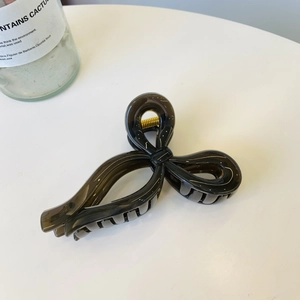Top view of a glossy black ribbon hair claw clip on a white table with cactus decor