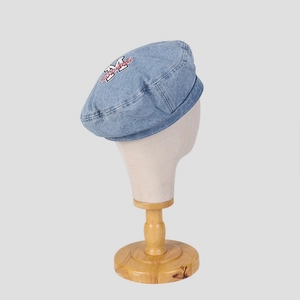 Detail of washed blue denim beret featuring vintage letter embroidery and patchwork design