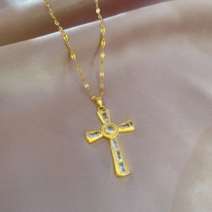 Macro shot of gold cross necklace featuring baguette and round cut clear zircon stones