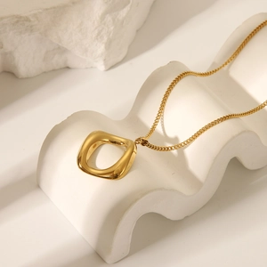 Detailed view of a gold heart pendant necklace displayed on a white wavy pedestal
