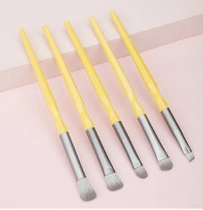 Detail of 5-piece makeup brush set with yellow geometric handles on pink stairs