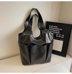 Large black shoulder tote bag with three front pockets shown in a minimalist studio setting