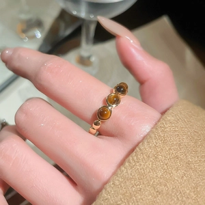 Détail de trois pierres œil de tigre brunes sur une bague ouverte plaquée or au doigt