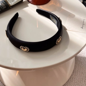 Detailed macro view of black satin headband with gold heart motifs and handmade label