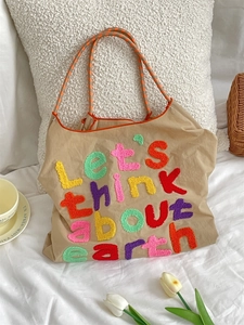 Detail of khaki canvas tote bag with colorful towel embroidered letters and woven straps