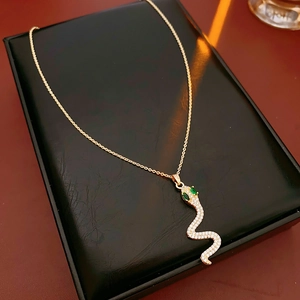 Dettaglio della collana a serpente dorata con zirconi e gemme verdi su scatola nera