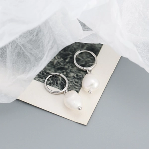 Detailed shot of silver s925 hoops with natural white baroque pearl charms on dark card