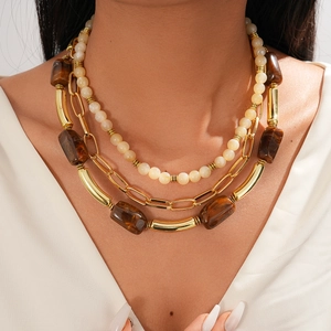 Bohemian multilayer necklace with beige beads and gold chain links on a model neck