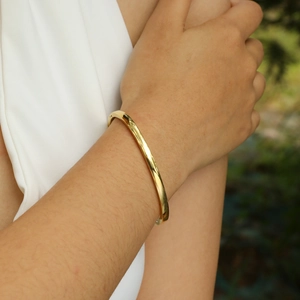 Close-up of polished gold-finished stainless steel bangle bracelet on wrist