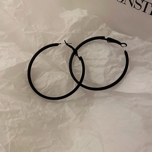 Detailed view of large black hoop earrings with silver pins on a textured paper background