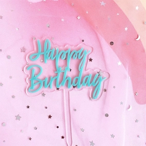 Detail of teal Happy Birthday acrylic cake topper over a dreamy pink tulle background