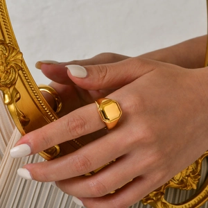 Close-up of a chunky gold signet ring on a model hand with a vintage frame backdrop