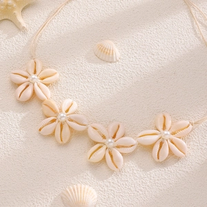Primo piano di collana bohémien con fiori di conchiglia e perle su sfondo di sabbia