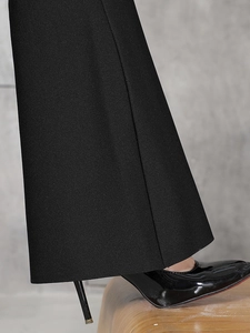 Gros plan du bas de pantalon noir texturé associé à des talons en cuir verni noir
