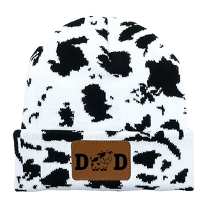 Detail view of cow print knitted beanie featuring a brown leather patch with DAD text