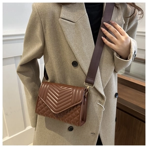 Detail van bruine gewatteerde crossbodytas met brede riem gedragen op een jas