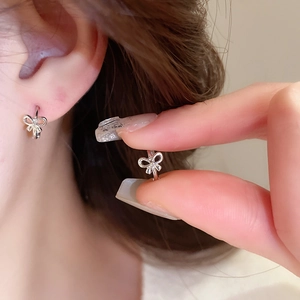 Detailed close-up of delicate silver bow-shaped hoop earrings worn by a model