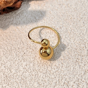 Minimalist gold-plated stainless steel ring with dual polished spheres on stone background