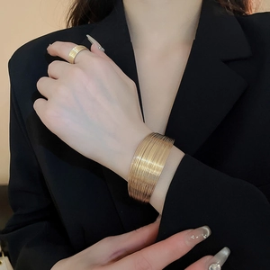 Close-up of a wide multi-layer gold metal bracelet and matching ring on a model