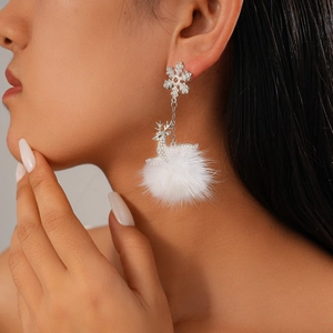 Close-up of snowflake and reindeer earrings with white fur balls worn by a model