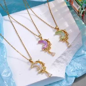 Three gold necklaces with colorful moon pendants and zircon teardrop charms on stone steps