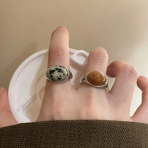 Close-up of Dalmatian Jasper and reddish-brown stone oval rings on finger