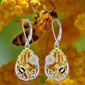Vista macro de pendientes de margarita con abeja dorada y detalle de gota de miel