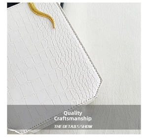 Detail view of white crocodile embossed leather bag with gold snake shaped metal buckle