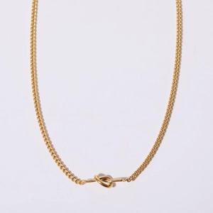 Detailed close-up of a golden love knot pendant on a stainless steel link chain necklace