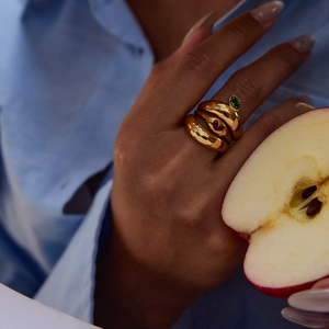 Artistic gold stacked rings with green gemstone and red heart detail on a model's hand