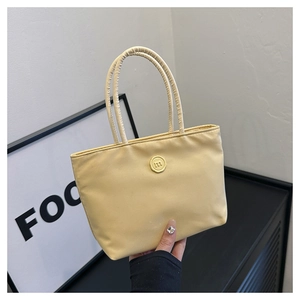 Détail du sac seau en nylon jaune avec badge rond et lettre M en relief sur le devant