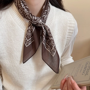 Close-up of a brown paisley print silk scarf necklace styled with a beige knit vest