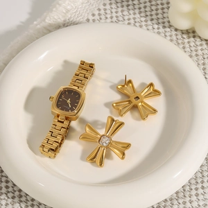 Macro detail of gold cross earrings with zircon and a square fashion watch on a tray