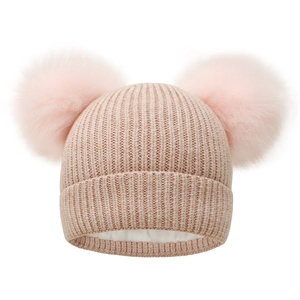 Detail of pink knitted winter hat featuring faux fur pom-poms and warm fleece lining