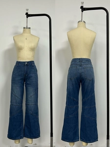 Detail of high-waisted blue denim jeans showing curved patchwork seams and washed texture