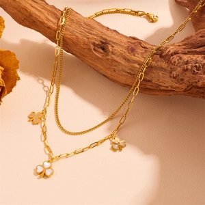 Double-layered gold clover necklace with white mother-of-pearl inlay on wooden stand
