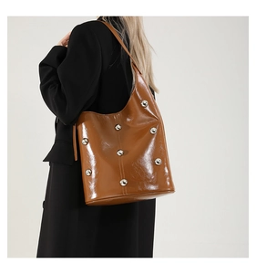 Close-up of brown leather shoulder bag with glossy finish and silver round metal studs