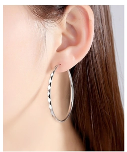 Detailed close-up of large 925 silver hoop earrings with textured diamond-cut surface